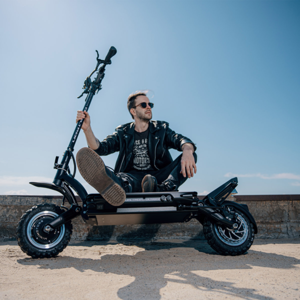 Man in leather jacket sitting behind the Dualtron Ultra 2 electric scooter on a sandy beach, showcasing an urban lifestyle.