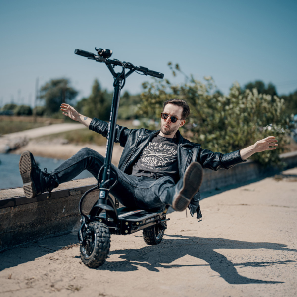 Man sitting on the Dualtron Ultra 2 electric scooter by the water, arms spread out for balance, enjoying a relaxed moment outdoors.