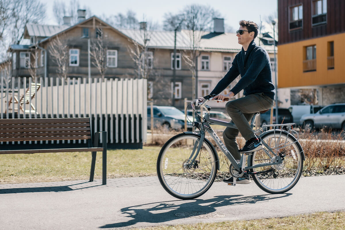 Image of man riding Electric bike Oolter eke in the city sidewalk with houses on the background.