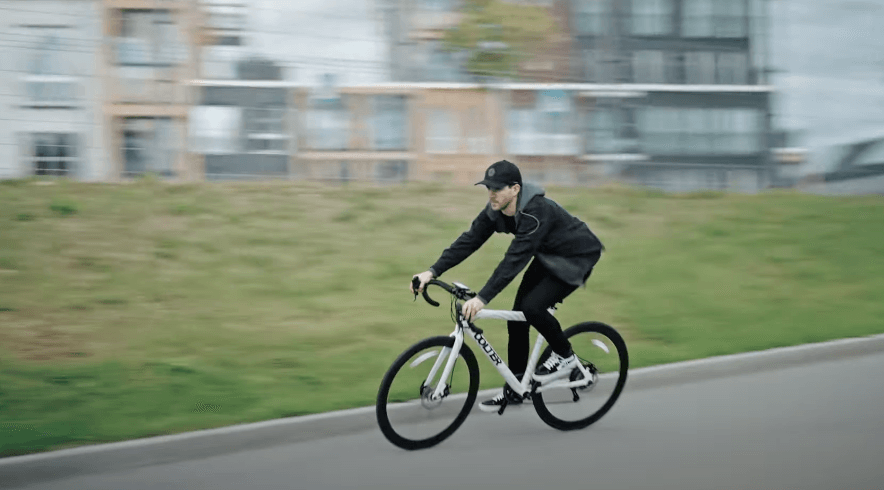 Man riding a white Oolter Torm electric bike at speed on an urban road, motion blur in the background emphasizing velocity and agility.