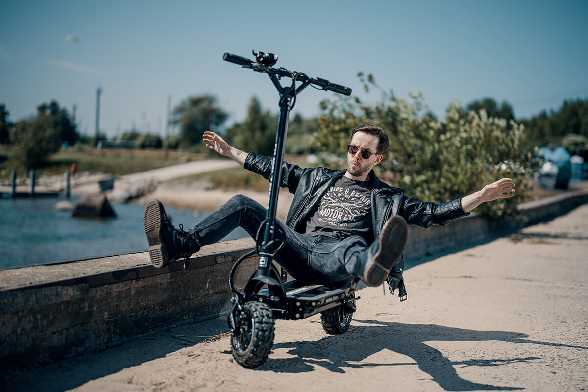 Man sitting casually on Dualtron Ultra 2 electric scooter at the beach, showcasing rugged off-road design and laid-back lifestyle