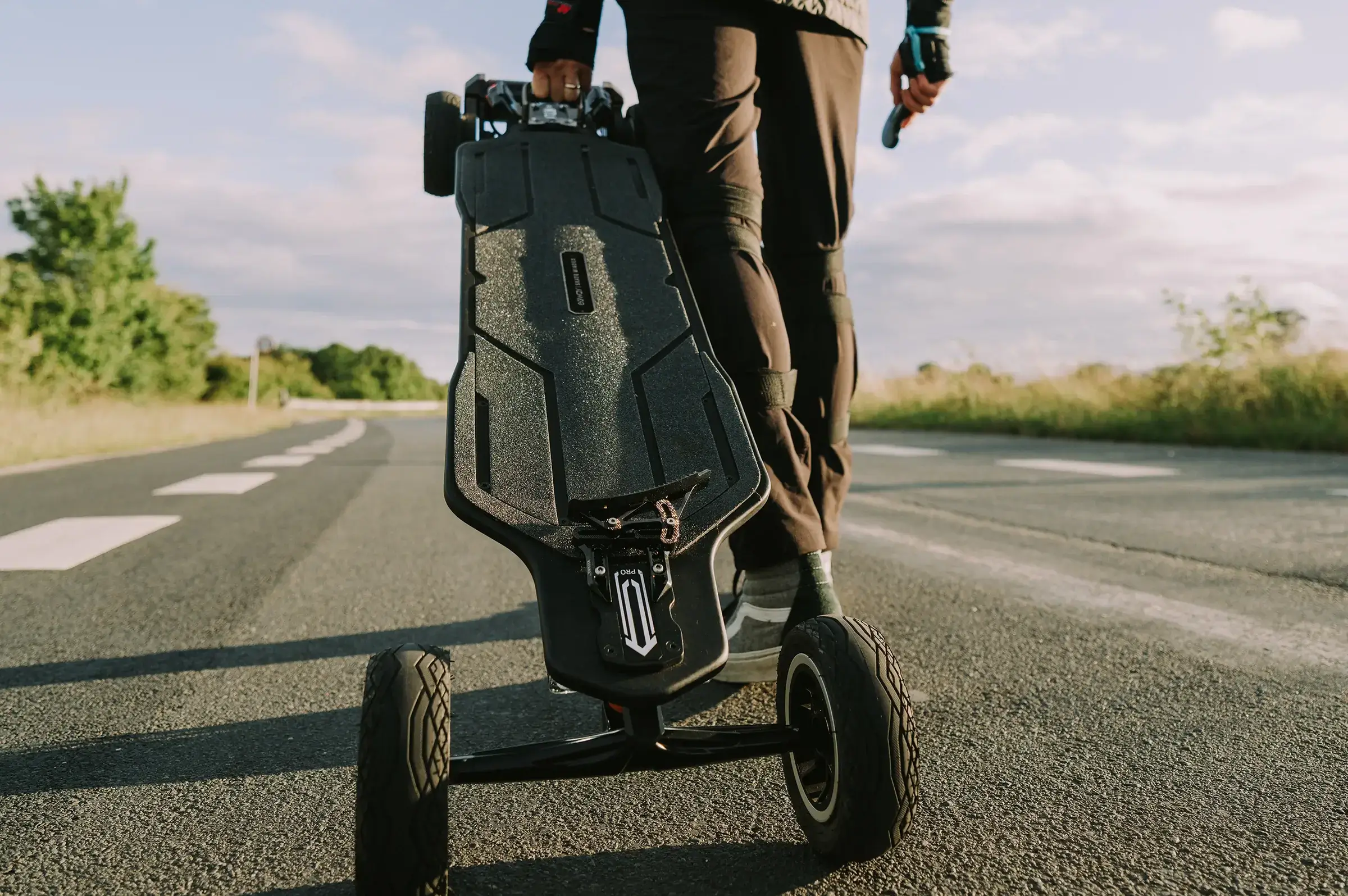 A person carrying the Exway Atlas Pro 4WD electric skateboard by its rear wheels while walking on the road.