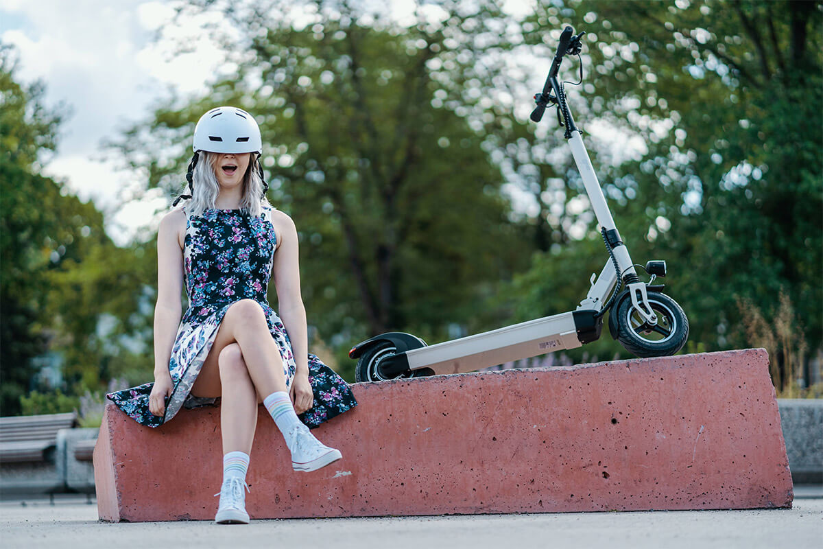 Image of a teen girl sitting at the skate park with a helmet covering her eyes and Electric scooter gpad joyride eco in the background.