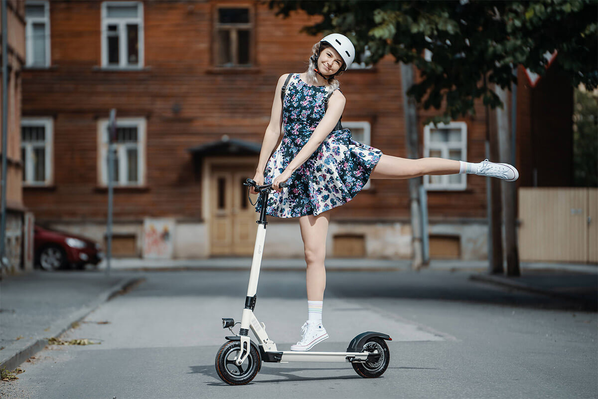 Electric scooter gpad joyride woman ballerina Image of woman standing on one foot on the electric scooter gpad joyride in the city street with wooden house on the background