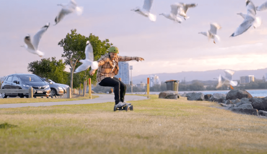 Rider cruising Evolve GTR 2 Bamboo All Terrain electric skateboard across grass with seagulls in flight