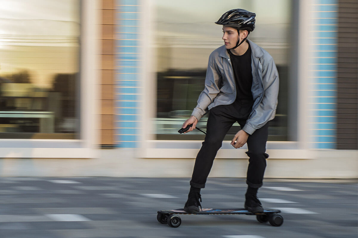 Electric skateboard GPad Blade urban riding Image of a young man riding Electric skateboard GPad Blade in the street in front of big shop windows wearing a helmet.