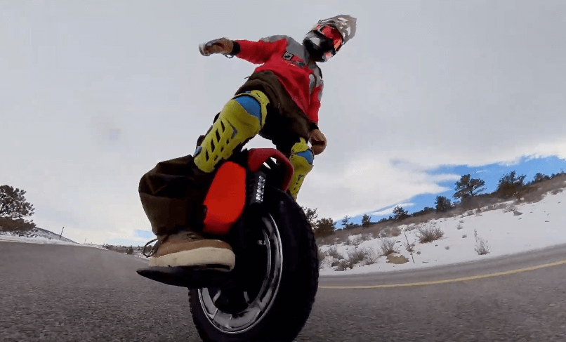 Fully geared rider leaning into turn on Kingsong KS S22 Pro+ electric unicycle on open mountain road