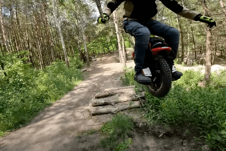 Rider jumping over trail logs on Kingsong KS S22 Pro+ electric unicycle in forest setting