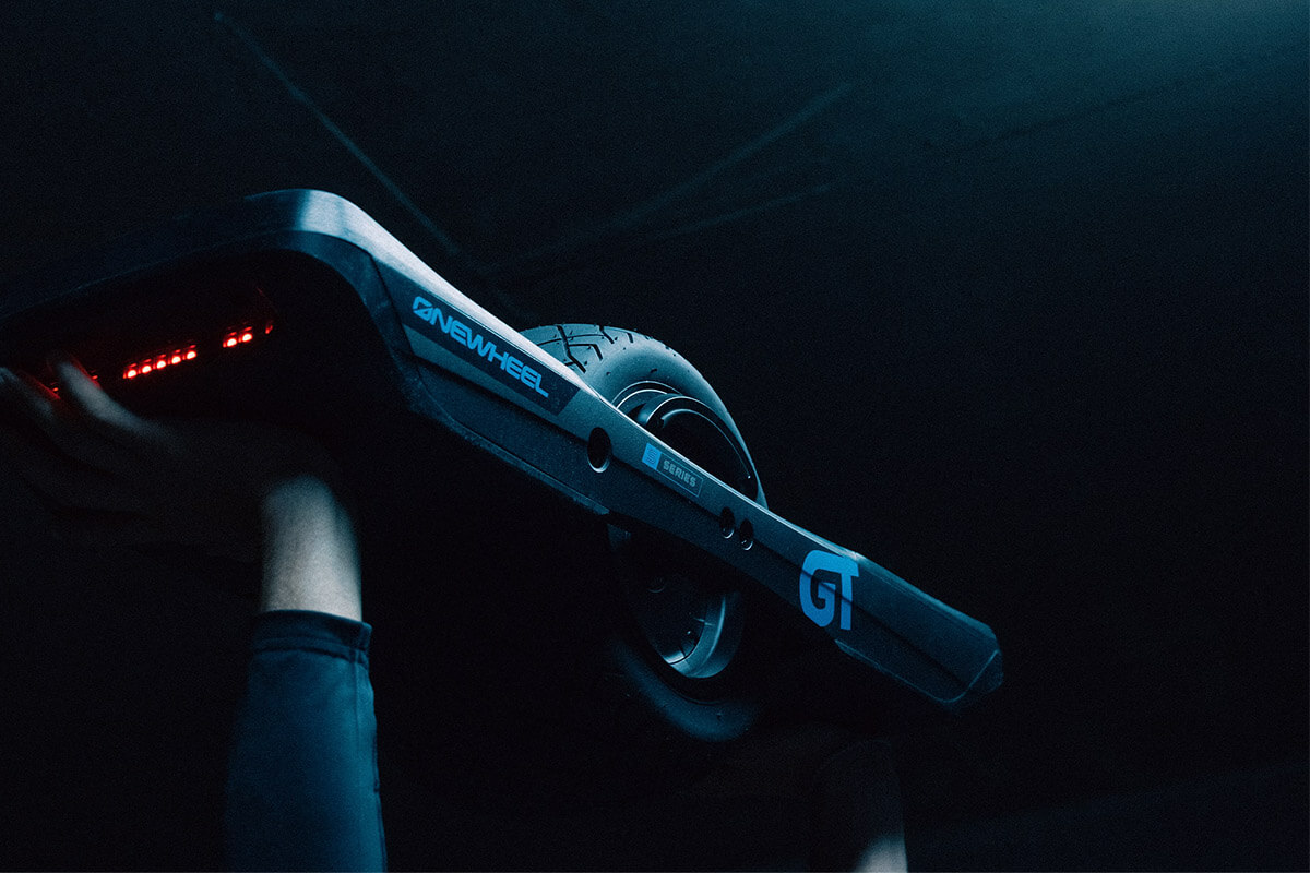 Onewheel GT S Series electric unicycle on raised hands on dark background.