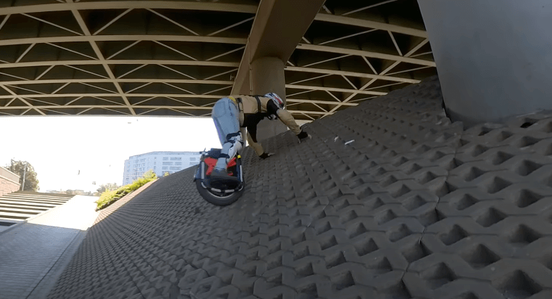 Rider pushing electric unicycle Veteran Sherman Max up a steep concrete embankment under a bridge in urban environment