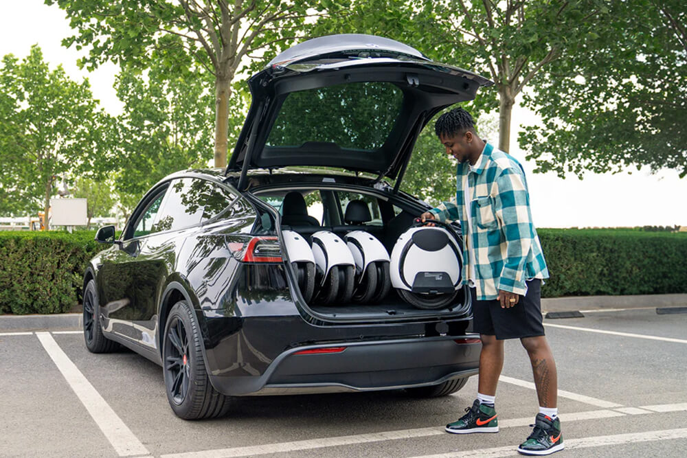 Inmotion E20 car storage Person loading the Inmotion E20 electric unicycles into the trunk of a black car parked outdoors, demonstrating easy transport and storage.