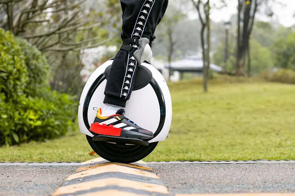 Inmotion E20 speed bump Close-up of a person riding the Inmotion E20 electric unicycle over a speed bump in a park, highlighting the vehicle’s balance and agility.