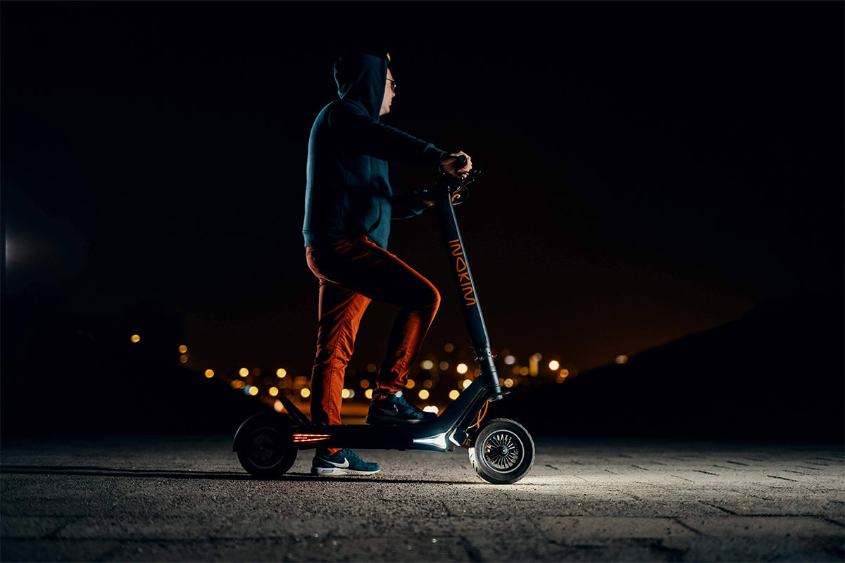 Man standing with Inokim OX Hero electric scooter at night – LED lights on deck