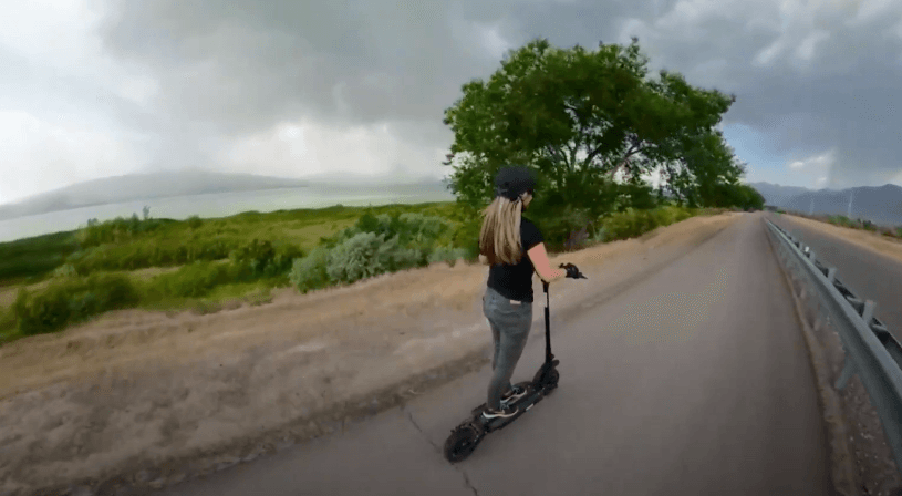 Woman riding Electric scooter Speedway Leger Eco in action near lake and forest on the road.