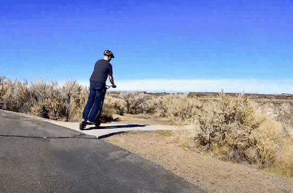 Rider cruising on Speedway Leger Eco electric scooter along a scenic desert trail under clear blue sky