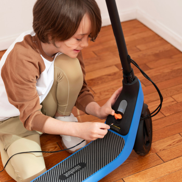 Electric scooter Segway C2 Lite being charged with power cable connected, showcasing compact and child-friendly design.