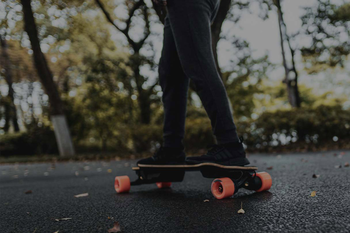 Man riding Electric skateboard Exway Flex ER Hub viewed from the side and riders legs and board are visible.