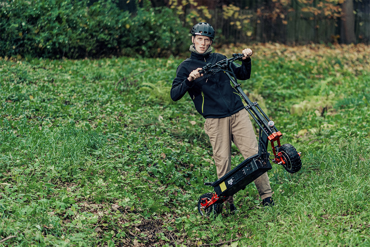 Man holding GPad F3 Max DT electric scooter on a grassy forest slope, demonstrating off-road build and suspension.