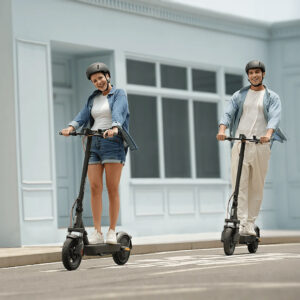 Nuori pariskunta ajamassa Xiaomi-sähköpotkulautoilla kaupunkikadulla kypärät päässä