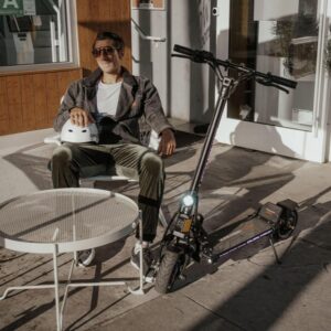Man relaxing outside with Dualtron Mini Special LB Dual Motor electric scooter parked beside him.