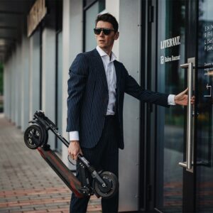 Man in business suit carrying folded E-TWOW S2 ECO electric scooter – ideal for commuting and portability.