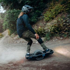 Mies ajamassa Onewheel GT S Rally Edition -sähköyksipyörällä metsässä, täyskypärä päässä