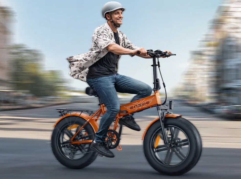 Engwe EP-2 Boost man riding A smiling man wearing a helmet rides an orange Engwe EP-2 Boost E fat-tire electric bicycle through a city street, with the background blurred to show motion.