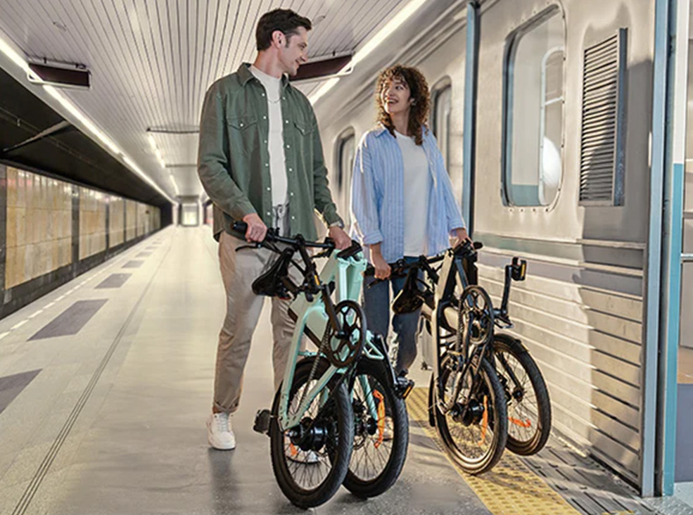 Engwe P20 electric bikes folded in train station Man with folded mint Engwe P20 and woman with folded black Engwe P20 electric bike in the train station