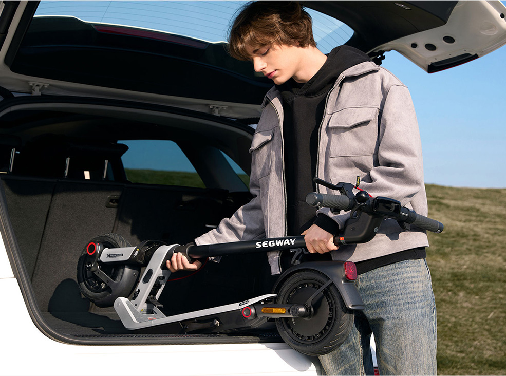 Segway-Ninebot E3 Pro E foldability Person loading a folded Segway-Ninebot E3 Pro E electric scooter into the trunk of a car, illustrating the scooter’s compact and portable design.