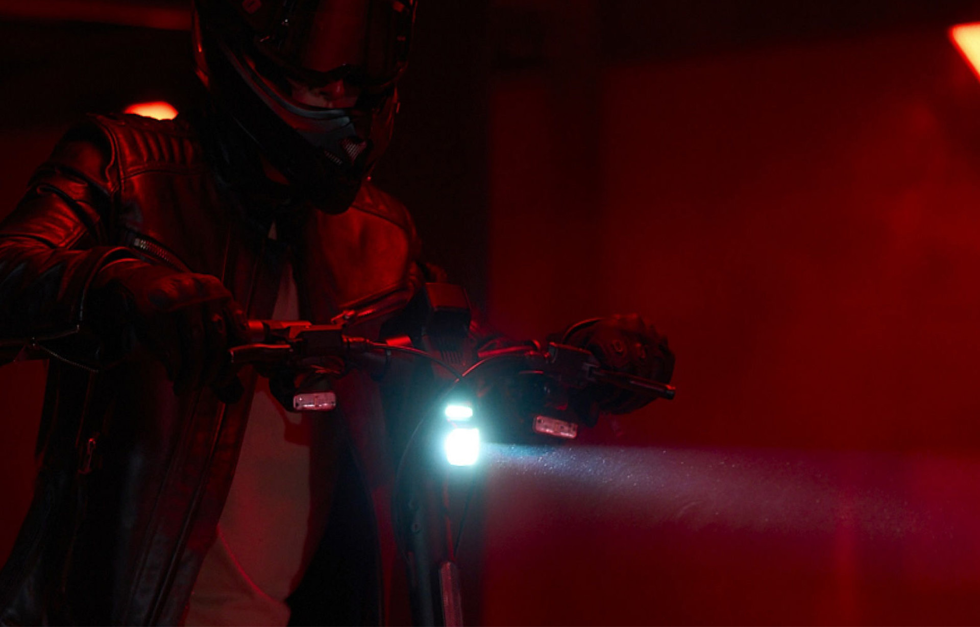 Close-up of the Segway-Ninebot GT3 Pro electric scooter’s bright front headlight shining in a dark red-lit setting.