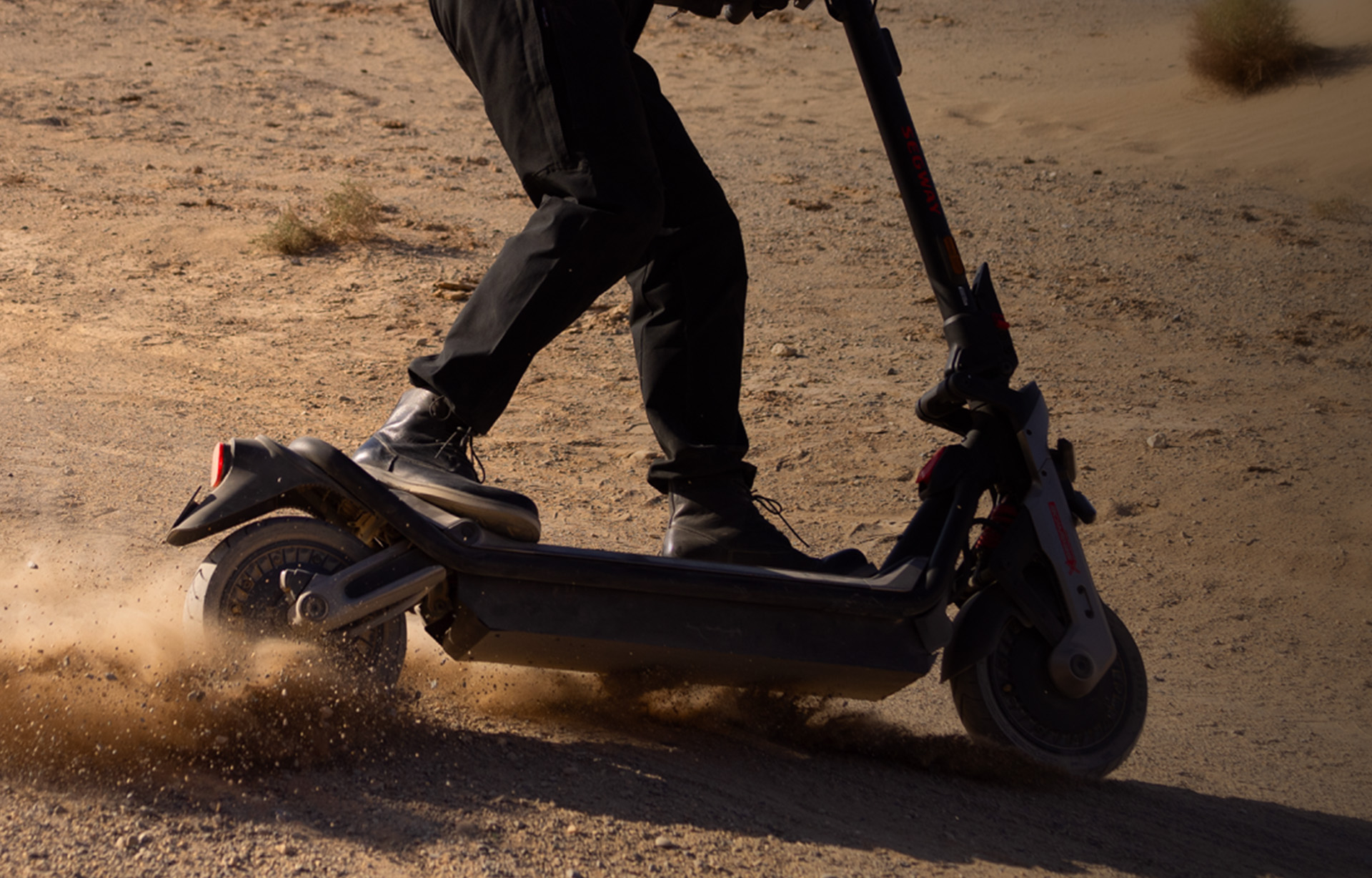 Rider testing the Segway-Ninebot GT3 Pro electric scooter’s stability enhancement system on a sandy off-road surface, with dust kicking up from the rear wheel for traction control.