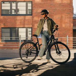 Külgvaade naisest, kes seisab kiivrit kandes linnatänaval Tunturi eMotion elektrijalgrattaga.