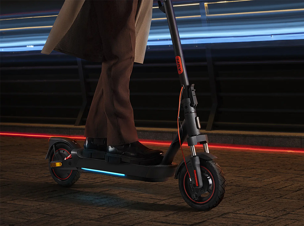 Person riding the Xiaomi 5 Max electric scooter during the night demonstrating the scooter's ambient light system.