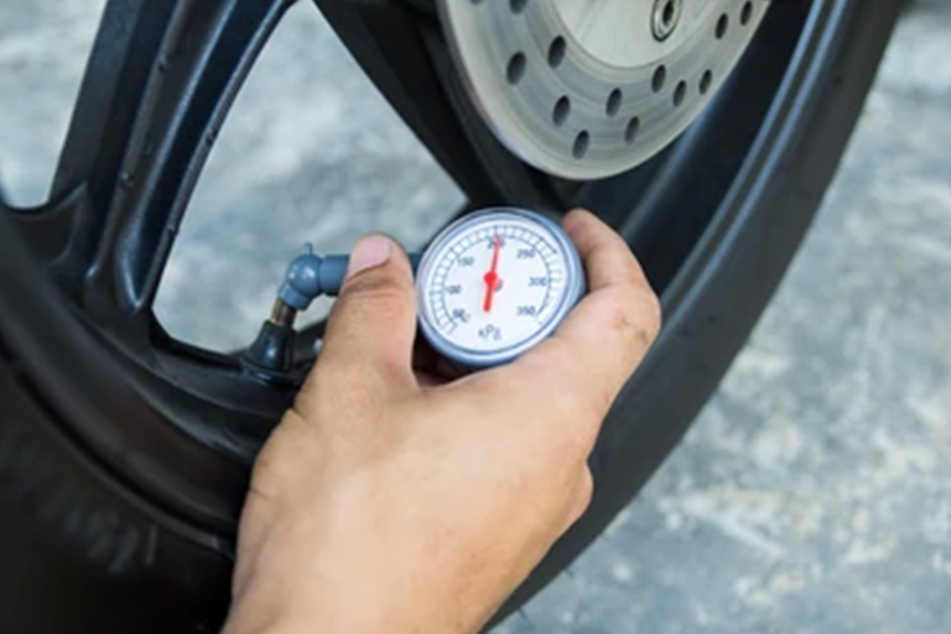 Tire pressure checking blog image A persons hand holds a tire pressure gauge against the valve of a wheel to check air pressure.