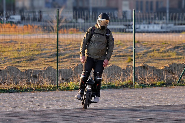 A rider wearing a helmet and knee pads riding an electric unicycle on a paved surface outdoors