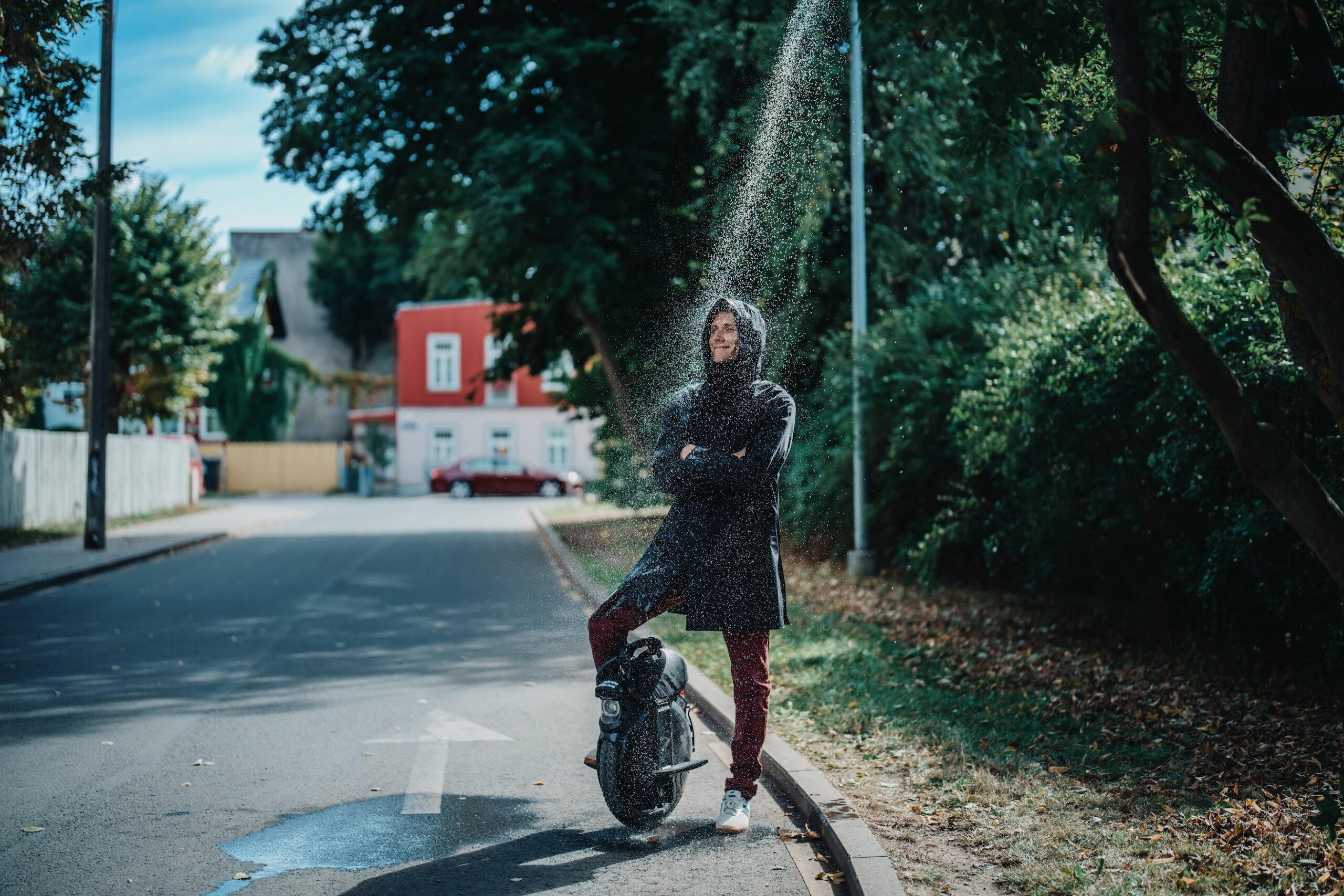 Person standing with an electric unicycle under water spray on a street