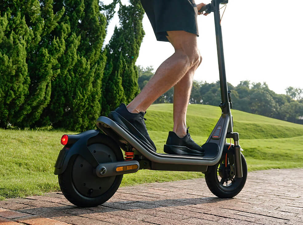 Close-up of a person riding the Xiaomi 6 electric scooter on a paved path in a green park setting.