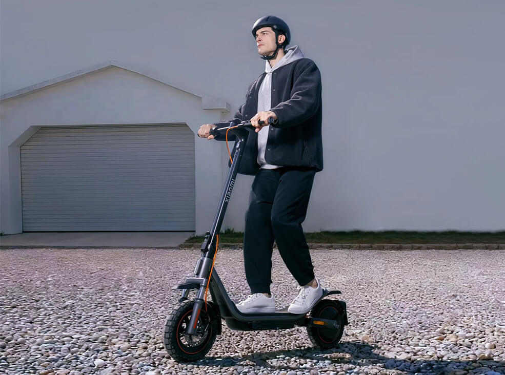 Man riding Xiaomi Scooter 6 Pro electric scooter on gravel while wearing a helmet and casual clothing.