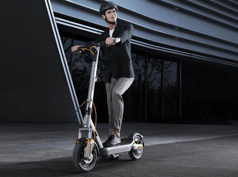 Xiaomi Scooter 6 Max lifestyle Rider standing with the Xiaomi Scooter 6 Max electric scooter in front of a contemporary office building.