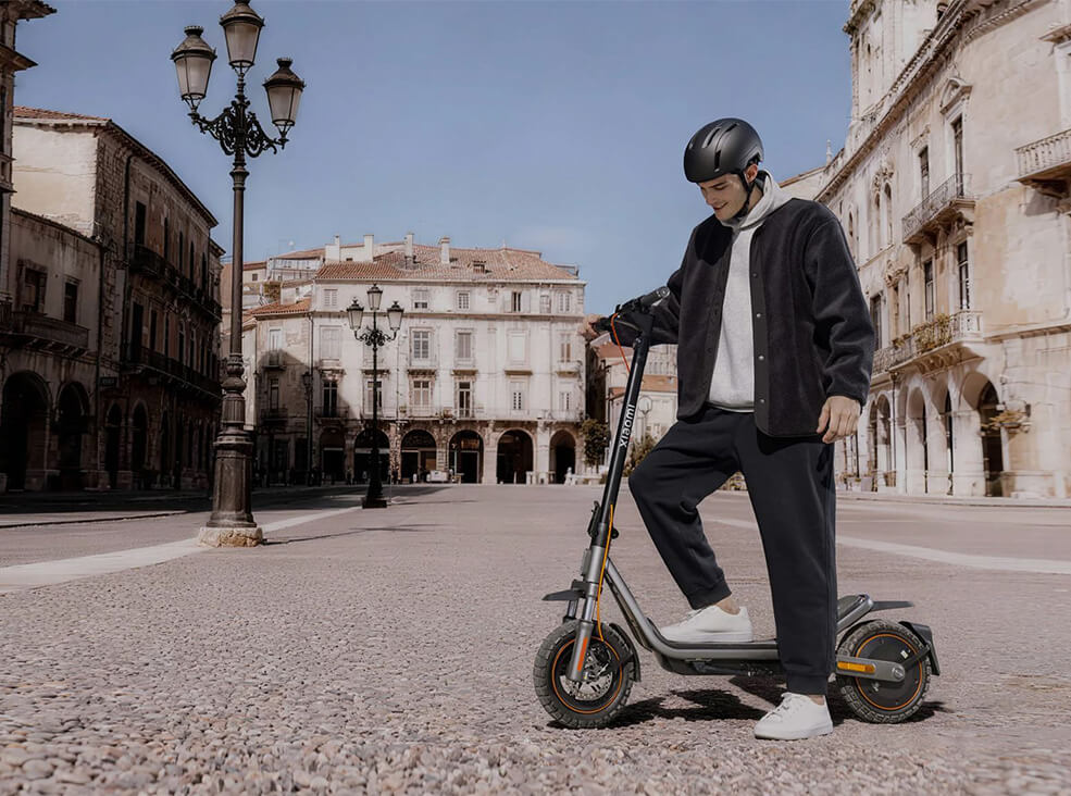 Man standing next to the Xiaomi Scooter 6 Pro in the city center while wearing a helmet and casual clothing.