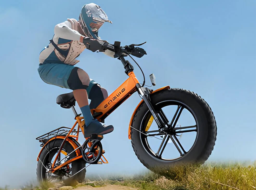 Person riding the orange ENGWE EP-2 Pro fat-tire electric bike off-road, performing a small jump on a grassy dirt trail while wearing a full-face helmet and protective gear against a clear blue sky.