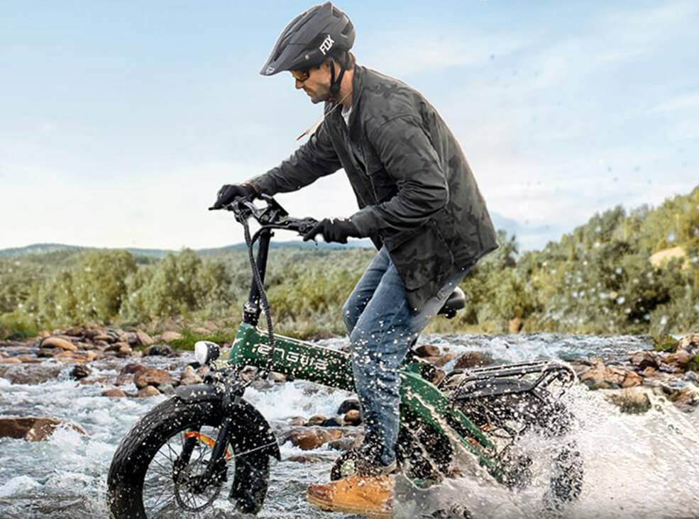 Rider crossing a shallow rocky stream on the Engwe EP-2 3.0 Boost folding electric bike, demonstrating its fat tires, front suspension, and capability on rugged off-road terrain.