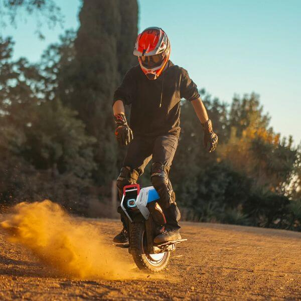 InMotion V14 Pro lifestyle Rider wearing a full-face helmet and protective gear riding an InMotion V14 Pro electric unicycle on a dusty off-road trail, kicking up a cloud of dirt while carving through a turn at sunset.