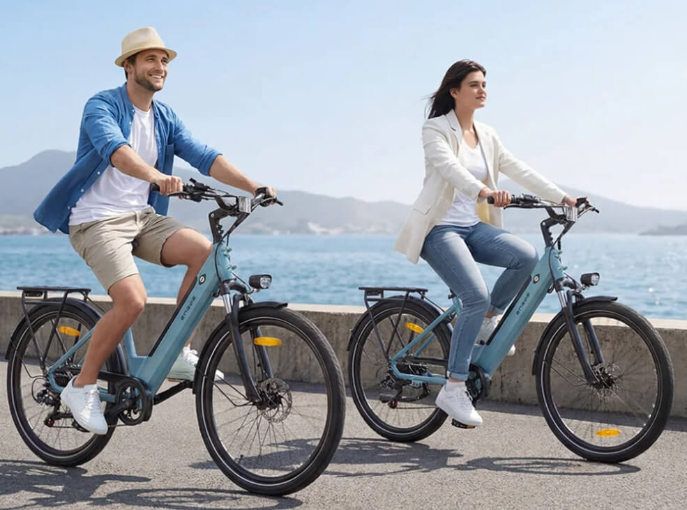 Man and woman riding sky blue ENGWE P275 SE electric bikes along a coastal promenade with sea and mountain views.