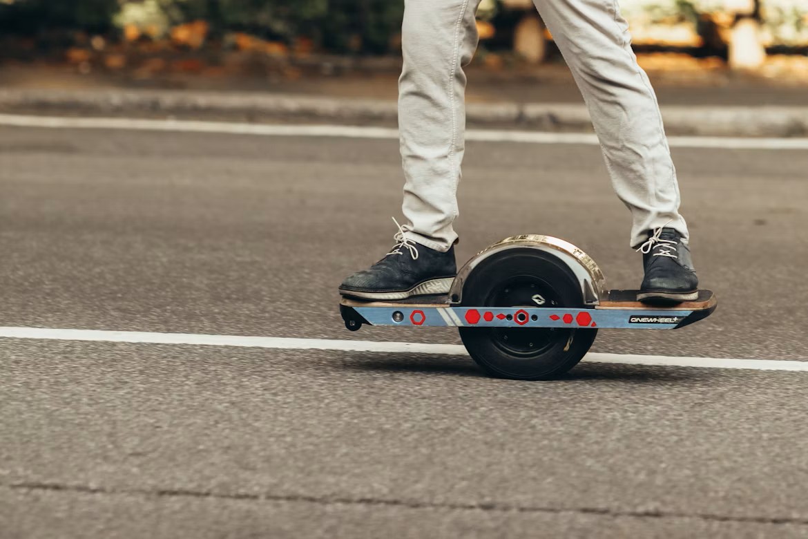 Close-up of a person riding a Onewheel electric board on a paved road.